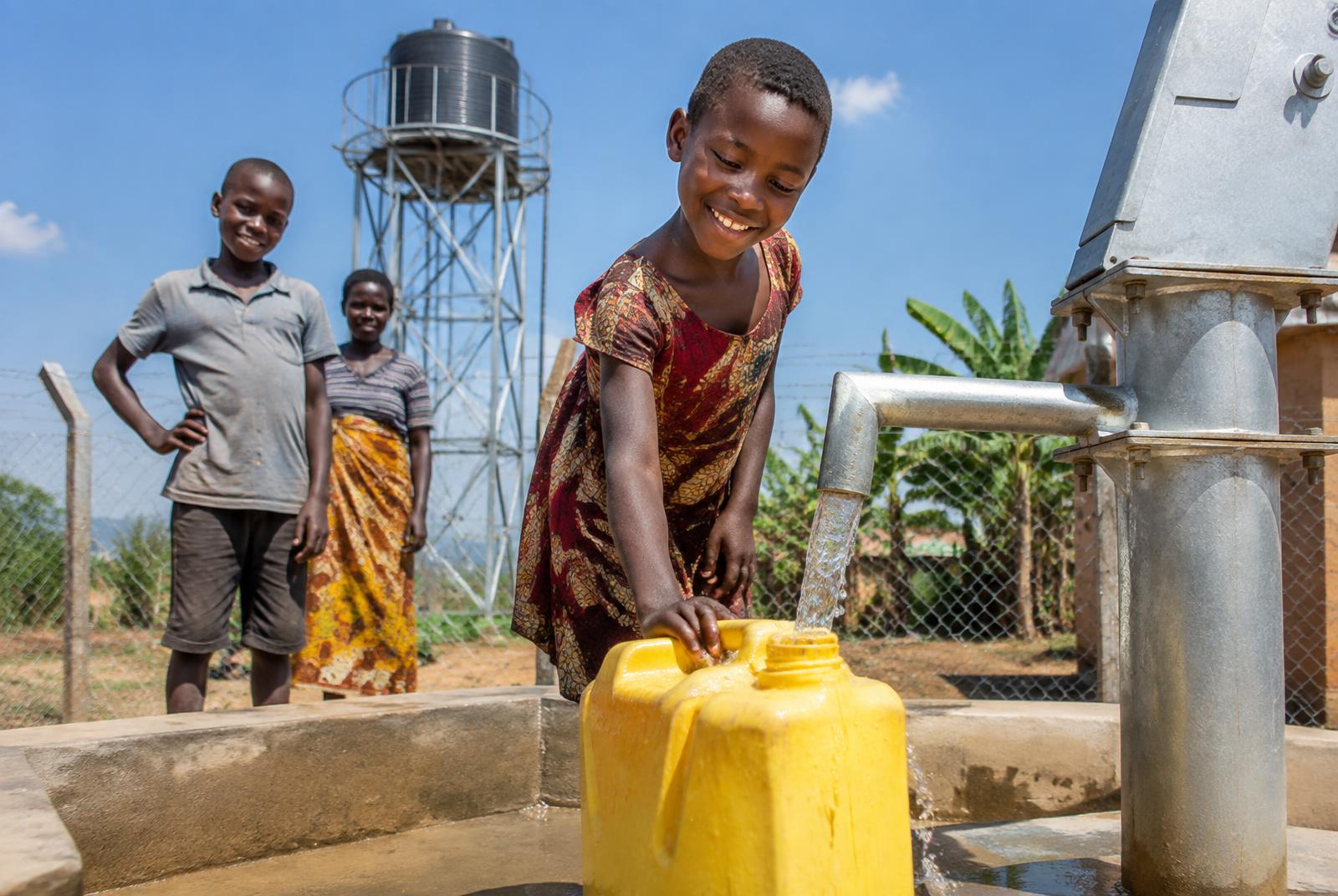 Clean water flowing from a borehole hand pump beside an elevated water tank
